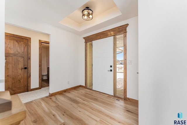 entryway with a tray ceiling and light wood-type flooring