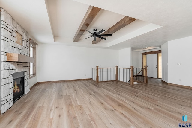 unfurnished living room featuring ceiling fan, a tray ceiling, a fireplace, light hardwood / wood-style floors, and beamed ceiling