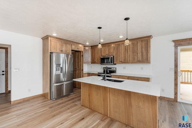 kitchen featuring pendant lighting, sink, light hardwood / wood-style flooring, a kitchen island with sink, and stainless steel appliances