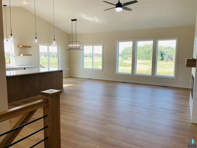 unfurnished living room with lofted ceiling, ceiling fan with notable chandelier, and light wood-type flooring