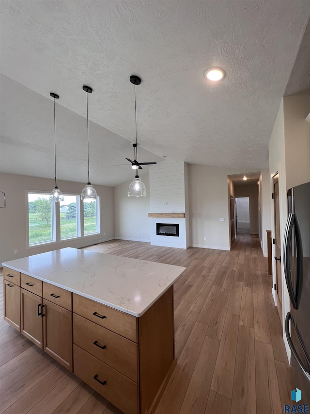 kitchen with black fridge, a fireplace, light hardwood / wood-style flooring, and pendant lighting