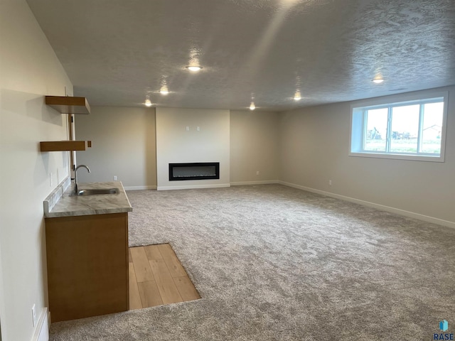 unfurnished living room with sink, carpet floors, and a textured ceiling