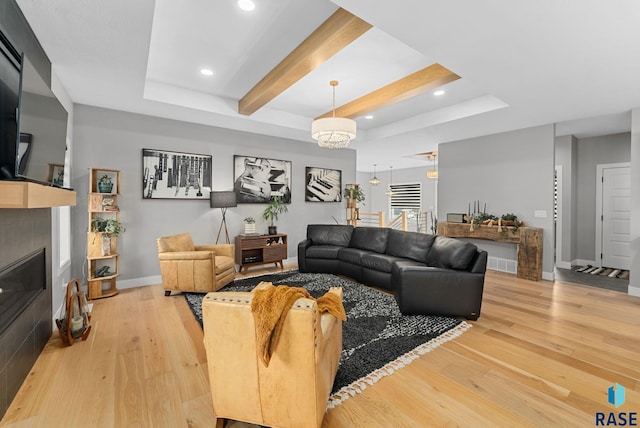 living room with beamed ceiling, a fireplace, light wood-type flooring, and a tray ceiling