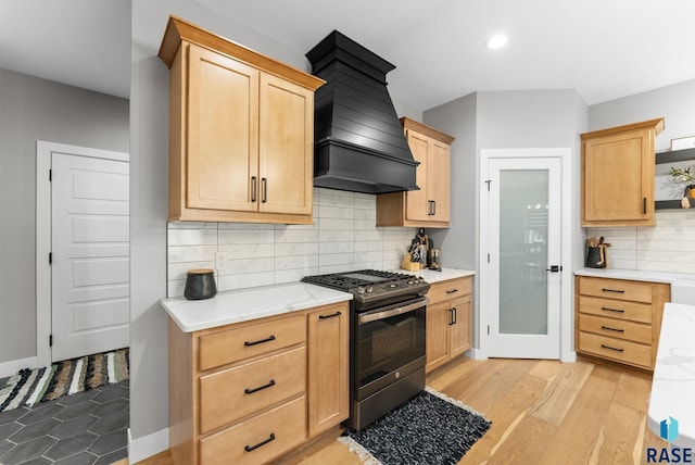 kitchen with light hardwood / wood-style flooring, light stone counters, stainless steel gas range oven, custom range hood, and light brown cabinetry