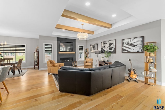 living room with a raised ceiling, a large fireplace, a chandelier, and light hardwood / wood-style flooring