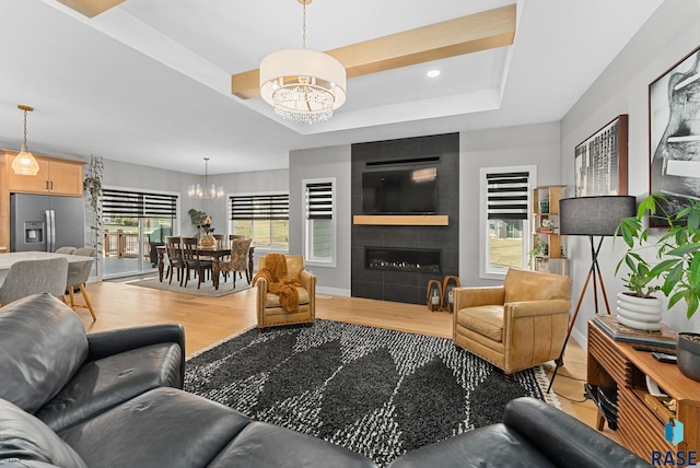 living room with a tiled fireplace, wood-type flooring, a chandelier, and a raised ceiling