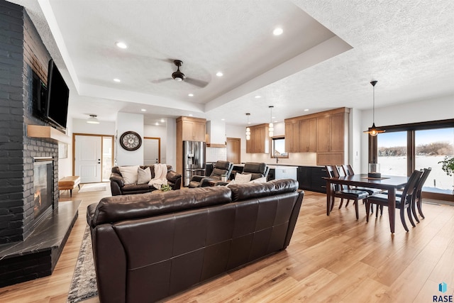 living room featuring a fireplace, a raised ceiling, light hardwood / wood-style floors, and a textured ceiling