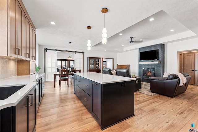 kitchen with hanging light fixtures, a center island, light hardwood / wood-style floors, a tray ceiling, and a barn door