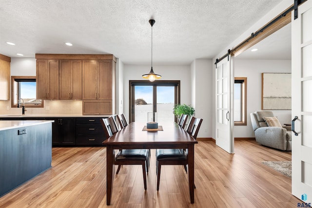 dining space with a barn door, sink, a textured ceiling, and light wood-type flooring