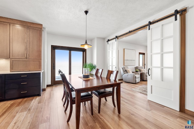 dining room featuring a barn door, a textured ceiling, and light hardwood / wood-style floors