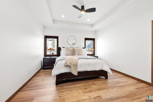 bedroom with a raised ceiling, ceiling fan, and light hardwood / wood-style floors