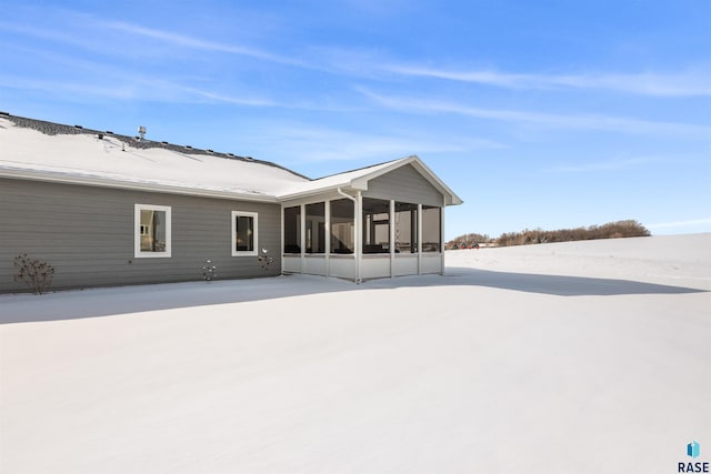 snow covered rear of property featuring a sunroom