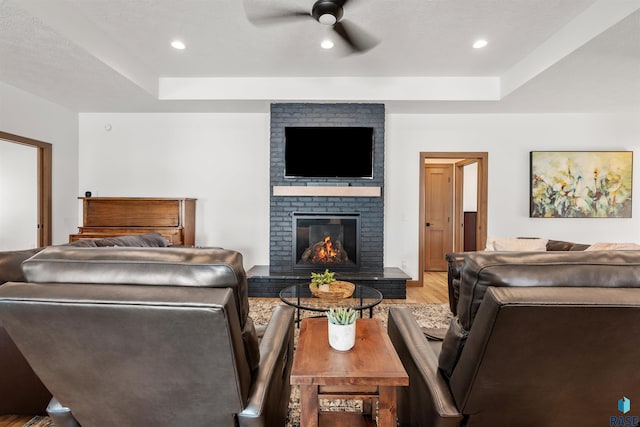 bedroom featuring ceiling fan, a tray ceiling, a brick fireplace, and light hardwood / wood-style flooring