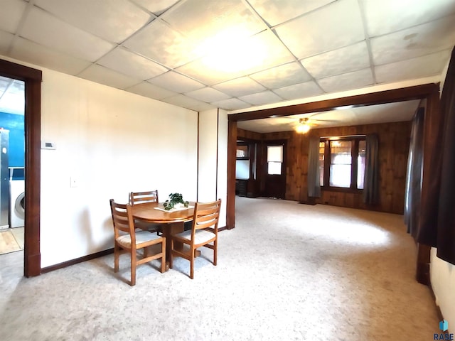 carpeted dining space with a drop ceiling, washer / dryer, ceiling fan, and wood walls