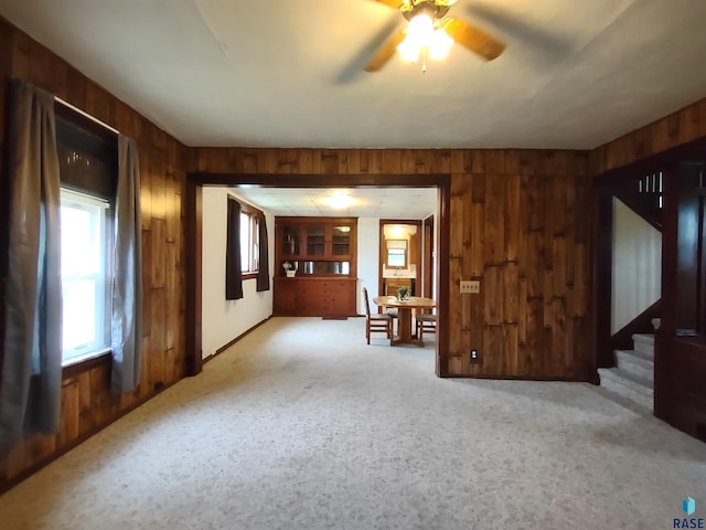 unfurnished living room with ceiling fan, light carpet, and wood walls