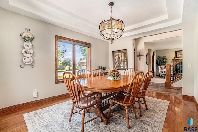 dining space with dark hardwood / wood-style floors, an inviting chandelier, and a tray ceiling