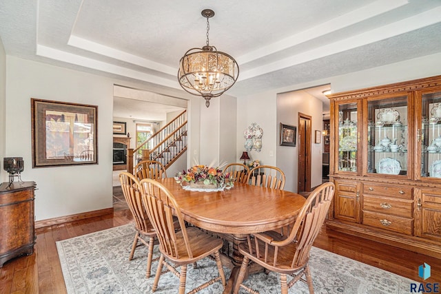 dining area featuring dark hardwood / wood-style floors, a raised ceiling, a textured ceiling, and a notable chandelier