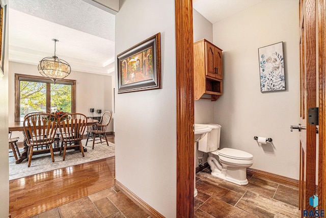 bathroom with a notable chandelier, a raised ceiling, and toilet