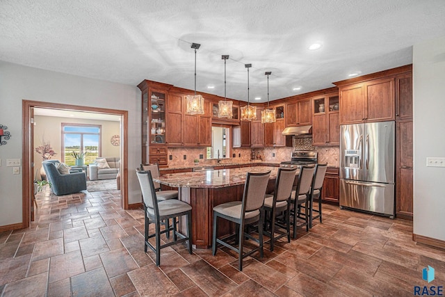 kitchen with backsplash, stainless steel appliances, a center island, light stone counters, and decorative light fixtures