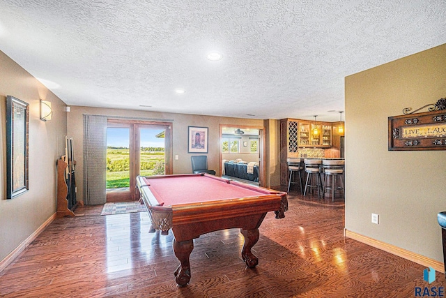 recreation room featuring indoor bar, pool table, a textured ceiling, and dark hardwood / wood-style flooring