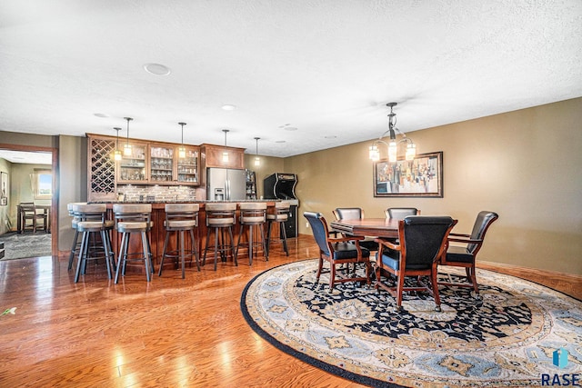 dining area featuring light hardwood / wood-style flooring, a textured ceiling, and bar area