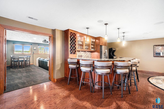 bar featuring dark wood-type flooring, light stone counters, stainless steel fridge, pendant lighting, and decorative backsplash