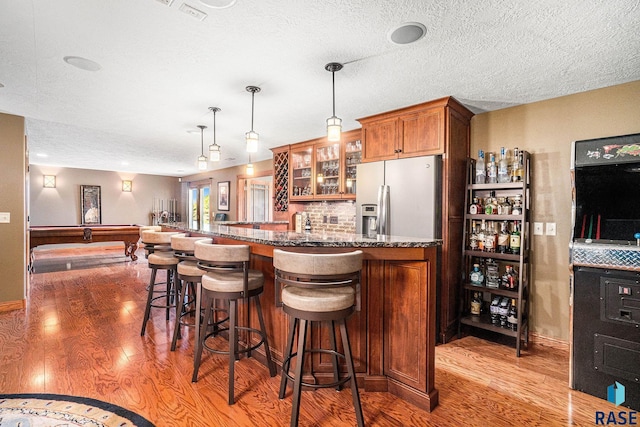 kitchen featuring pendant lighting, hardwood / wood-style flooring, a breakfast bar area, stainless steel fridge with ice dispenser, and dark stone counters