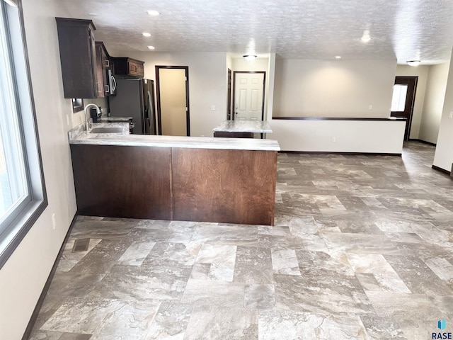 kitchen featuring sink, kitchen peninsula, black refrigerator with ice dispenser, and a textured ceiling