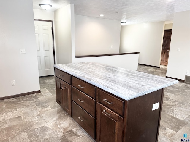 kitchen with dark brown cabinetry, light stone countertops, a center island, and a textured ceiling