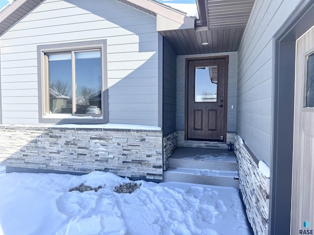 snow covered property entrance featuring stone siding