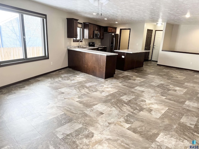 kitchen featuring appliances with stainless steel finishes, sink, kitchen peninsula, dark brown cabinets, and a textured ceiling