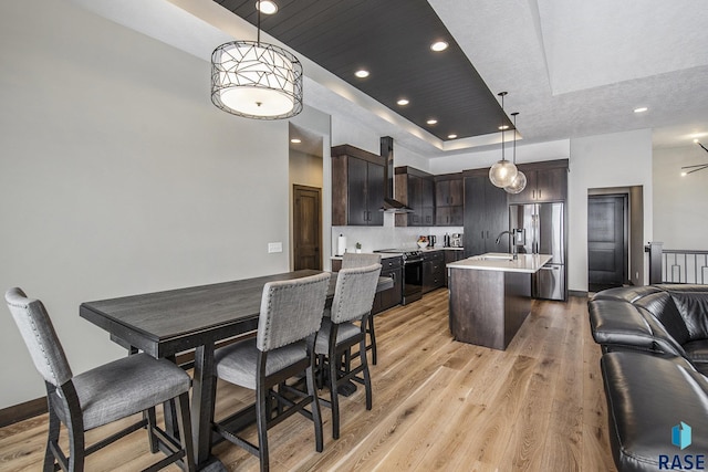 kitchen with decorative light fixtures, black electric range oven, a kitchen island with sink, dark brown cabinetry, and a tray ceiling