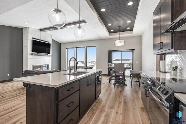 kitchen featuring an island with sink, sink, a large fireplace, hanging light fixtures, and wall chimney range hood