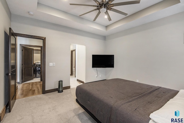 bedroom with a raised ceiling, light colored carpet, and ceiling fan