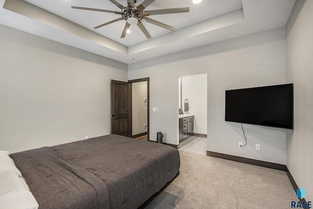 bedroom with light carpet, ensuite bath, a raised ceiling, and ceiling fan