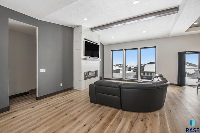 living room featuring vaulted ceiling with beams, a tiled fireplace, a textured ceiling, and light wood-type flooring