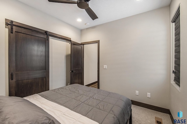 bedroom with a barn door, ceiling fan, and carpet