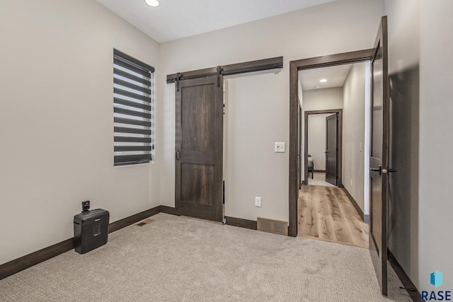 unfurnished bedroom with light colored carpet and a barn door