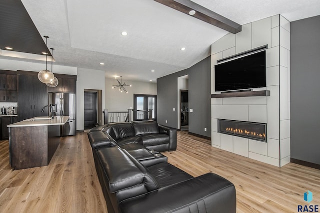 living room featuring a fireplace, lofted ceiling with beams, a notable chandelier, a textured ceiling, and light hardwood / wood-style flooring