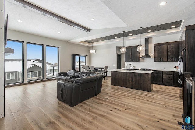 living room featuring sink, vaulted ceiling with beams, a textured ceiling, and light wood-type flooring