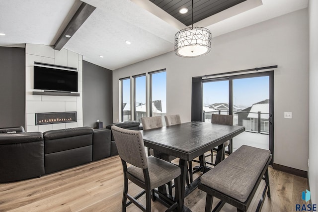 dining space with lofted ceiling with beams, a raised ceiling, a fireplace, and light hardwood / wood-style floors