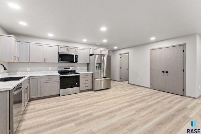 kitchen with appliances with stainless steel finishes, sink, gray cabinetry, and light hardwood / wood-style flooring