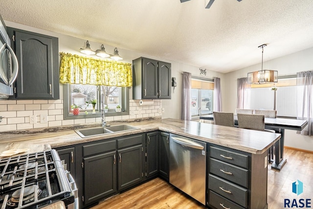 kitchen with appliances with stainless steel finishes, sink, hanging light fixtures, kitchen peninsula, and a healthy amount of sunlight