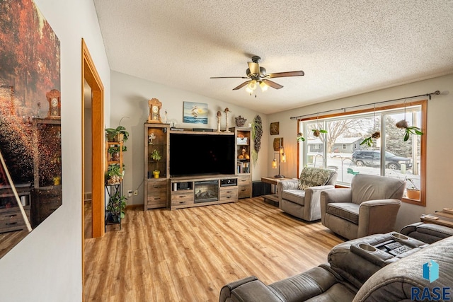 living room with ceiling fan, vaulted ceiling, a textured ceiling, and light wood-type flooring