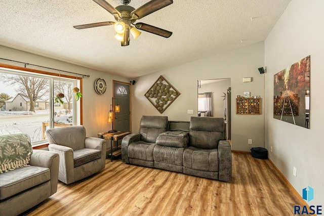 living room featuring vaulted ceiling, ceiling fan, a textured ceiling, and light wood-type flooring