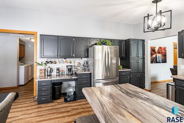 kitchen featuring pendant lighting, light hardwood / wood-style flooring, stainless steel refrigerator, independent washer and dryer, and a chandelier