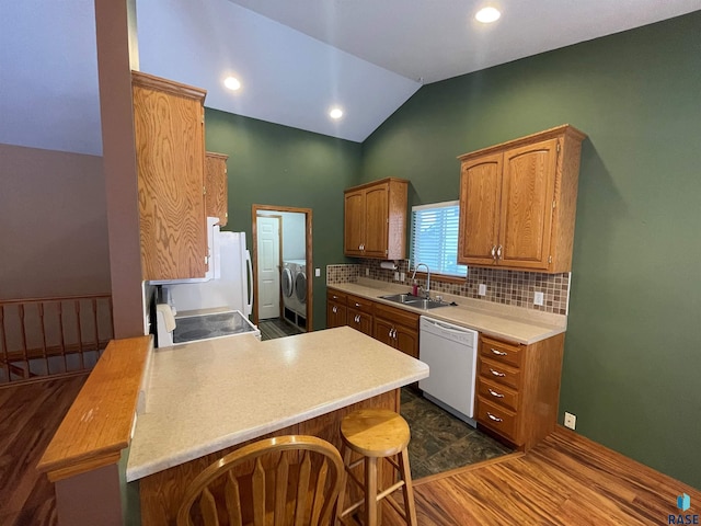 kitchen featuring sink, a kitchen breakfast bar, washing machine and clothes dryer, white dishwasher, and kitchen peninsula