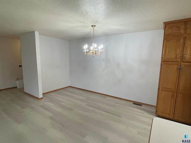 unfurnished dining area featuring an inviting chandelier, a textured ceiling, and light wood-type flooring