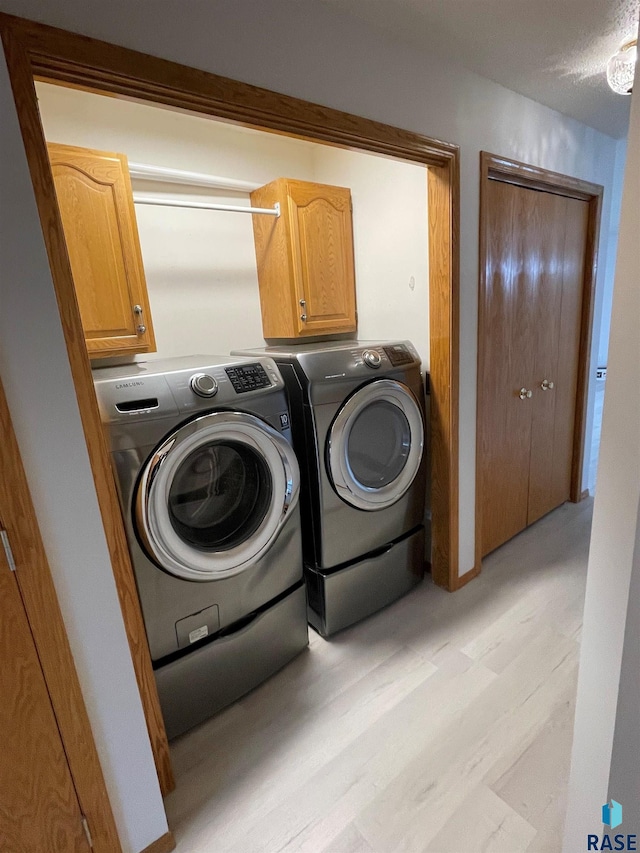 clothes washing area featuring independent washer and dryer, cabinets, and light hardwood / wood-style floors