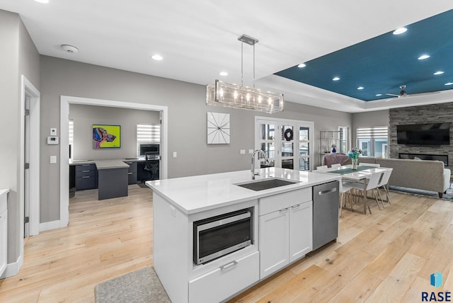 kitchen with decorative light fixtures, white cabinetry, sink, stainless steel appliances, and a center island with sink